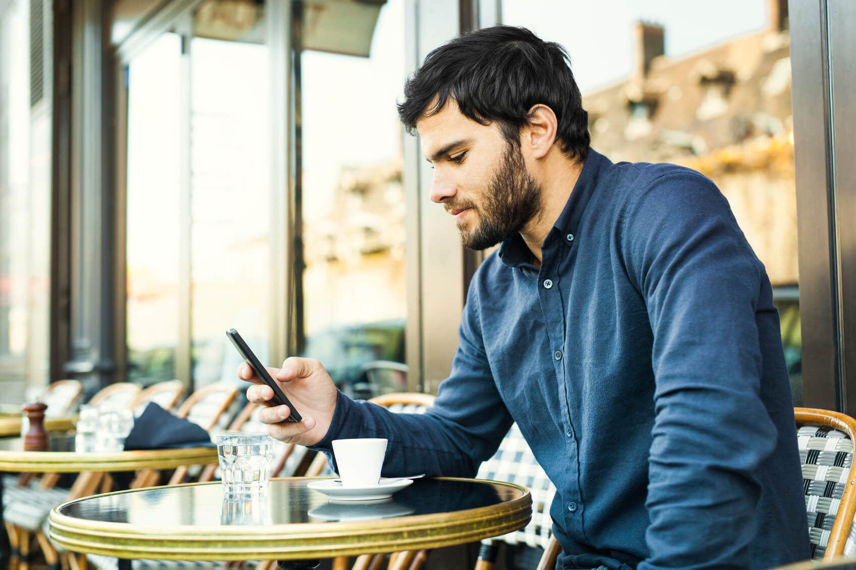 Young Man Browsing Social Media in a Sidewalk Cafe Man looking at cellphone