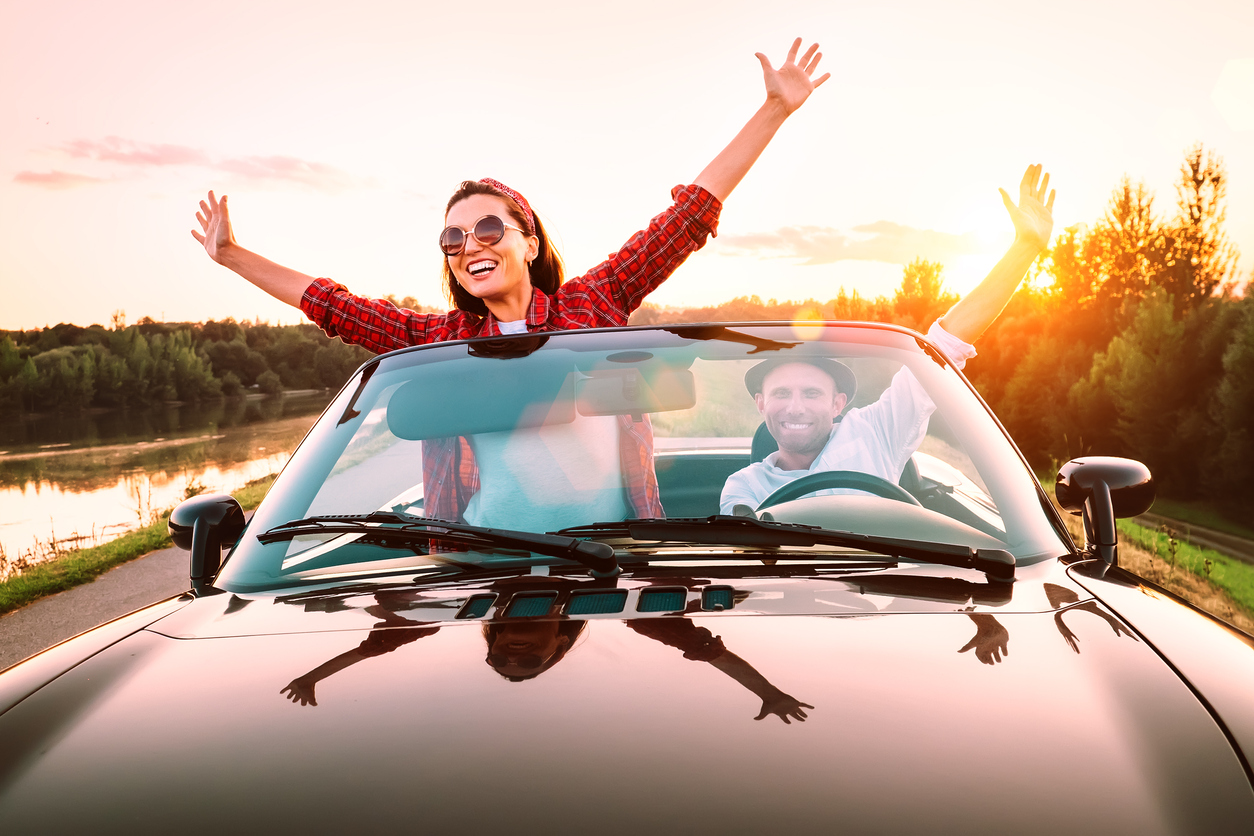 Traveling by car - happy couple in love go by cabriolet car in sunset time